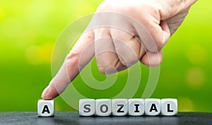 Hand moves a dice and changes the German word `asozial` asocial to `sozial` social.