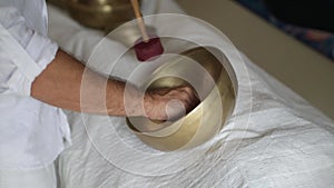 A hand moving a wooden stick along a border of a tibetan singing bowl during healing sound therapy