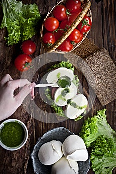 Hand with mozzarella and pesto sandwich, kitchen table with tomatoes, salad and dark bread, nobody