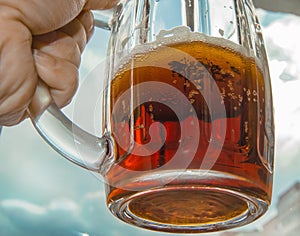 Hand with a mug of cold beer against the sky, close-up, bright light