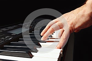 Hand of musician play the keys of the electronic organ on black background