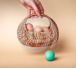 Hand with natural eggs in basket and outstanding Easter mint dyed one on beige background. Nutritious farm product and