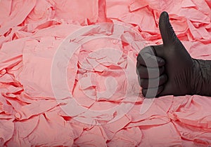 Hand in new black latex medical glove on background of a lot pink rubber gloves