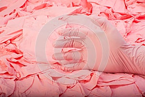 Hand in new pink latex medical glove on background of a lot pink rubber gloves