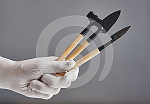 Hand in new pure white glove holding gardening tools isolated on gray background.