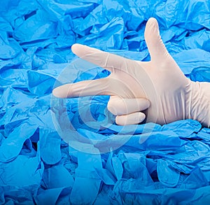 Hand in new white latex medical glove on background of a lot blue rubber gloves