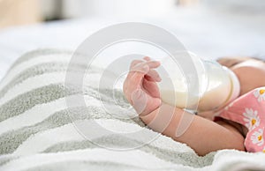 Hand of newborn baby holding and drinking milk from bottle alone on bed at home