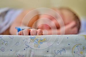 Hand newborn baby with a maternity hospital bracelet on his arm is sleeping in a crib. A newly born child in a clinic bed behind a