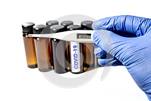 A hand in a nitrile glove holds a thermometer against the background of medical test tubes