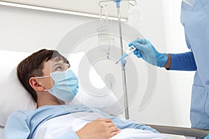 Hand nurse with thermometer measures fever on patient child in hospital bed, wearing protective surgical mask, corona virus covid