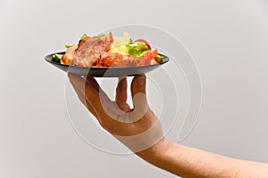 Hand of officiant hold the plate with meat dish bacon with potato and salad