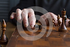 The hand of an old man puts a black king`s figure on the board acknowledging loss, concept business games, selective focus