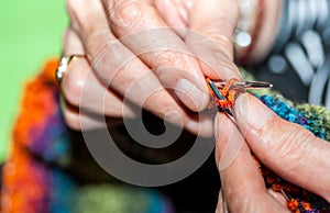 Hand of old woman holding knitting needles and multi colored wool for woolwork of warm sweater for cold winter days close up selec