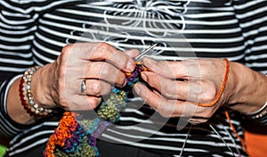 Hand of old woman holding knitting needles and multi colored wool for woolwork of warm sweater for cold winter days close up selec