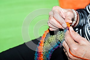 Hand of old woman holding knitting needles and multi colored wool for woolwork of warm sweater for cold winter days close up selec