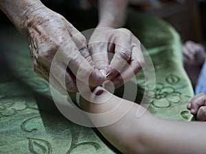 Hand of old woman waving a white string  Sai Sin  around her granddaughter hands - Thai traditional blessing from an elder one