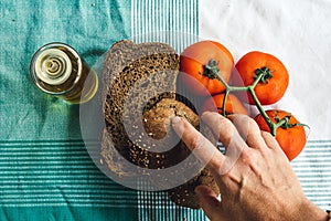 Hand on Olive Oil, tomato and brown bread on tablecloth