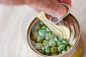 Hand open canned food in metal can on wooden background - Close up  peas canned goods non perishable food storage goods in kitchen