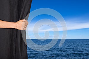 Hand opening black curtain with sea and sky behind it