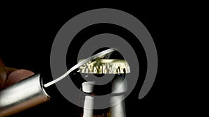 Hand opening cap on glass brown beer bottle. Macro shot of metal opener opening bottle on black isolated background in