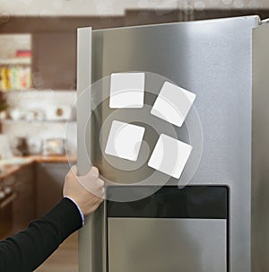 Hand opening gray refrigerator door with four blank white paper notes attached