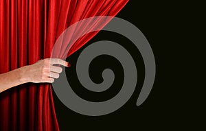 Hand opening red curtain over black background