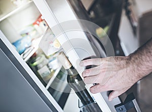 Hand opening refrigerator door in kitchen