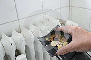 Hand is opening a wallet with few coins in front of an old, inefficient heater in a rental apartment, energy crises is increasing