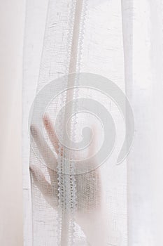 Hand opening white window curtains in room, closeup. Space for text. Bright morning sun through the curtains