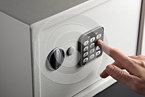 The hand opens a combination lock on the safe, a light safe on a dark background.