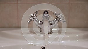 Hand opens the faucet in the washbasin in the bathroom.