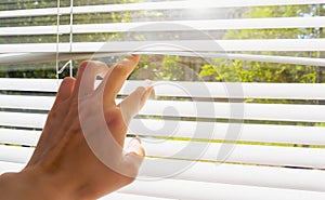 Hand opens with fingers blinds, outside window there is sunlight and green trees. Concept hot summer and scorching sun