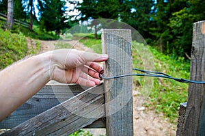 hand opens an old wooden gate. Against the background