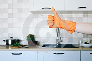 Hand in orange protective glove showing thumb up on kitchen background