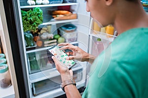 hand ordering groceries online via mobile phone apps with open fridge