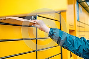 Hand with package. Send or receive parcel with yellow self service post terminal machine.