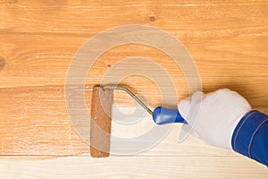 A hand with a paint roller paints a wooden surface with dark varnish, on top there is a place for inscription