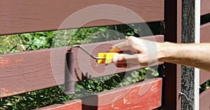 Hand with paint roller restoring old fence color