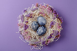 Hand painted dark blue easter eggs in nest and flowers on violet