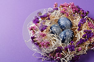 Hand painted dark blue easter eggs in nest and flowers on violet