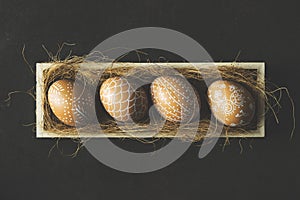 Hand painted easter eggs in wooden crate on black background, top view shot