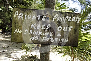 A hand-painted `keep out` sign near a tropical beach