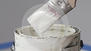 Hand of painter dipping a brush into a bucket with white paint. The paint drips from the brush into the bucket