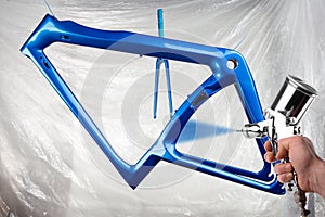 Hand of painter with spray gun producing a shiny new fresh paintwork coating paint of a metallic blue carbon racing road bicycle