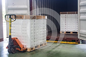 Hand pallet truck loading shipping boxes and goods on wooden pallet at loading dock from container.Soft focus