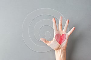 Hand palm of young Caucasian woman girl with painted on red heart on gray wall background. Charity love donation Valentine health