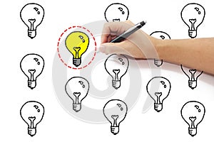hand with pen drawing selected red dash circle around yellow light bulb idea among many on pure white background.