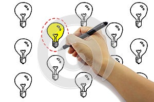 hand with pen drawing selected red dash circle around yellow light bulb idea among many on pure white background.