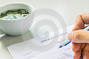 Hand with pen over application form with tea cup