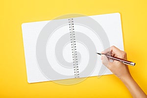 Hand with pen over blank notebook on a yellow background. Mock up with copy space for your ideas